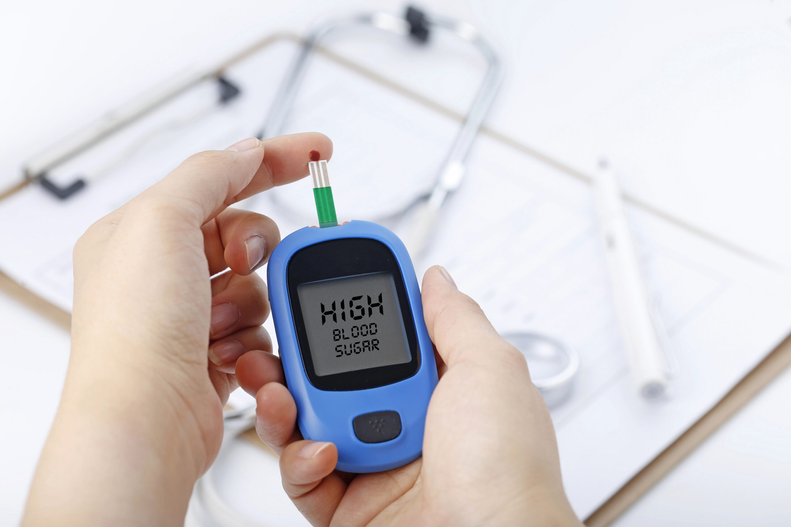 hand holding a blood glucose meter measuring blood sugar, the background is a stethoscope and chart file